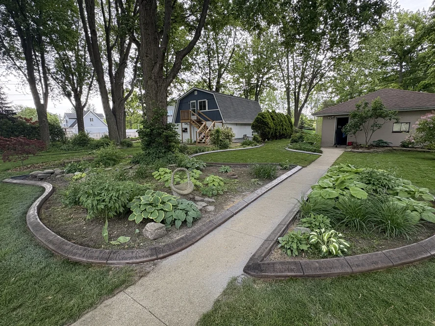 Brown stamped concrete curbing framing garden beds on either side of a walkway leading to a backyard studio.