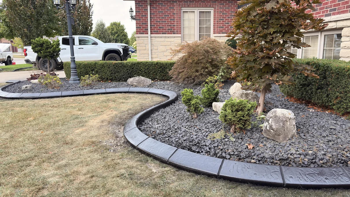 Dark charcoal stamped concrete curb along a large lava-rock bed with a Japanese maple, accent boulders and lamp post.